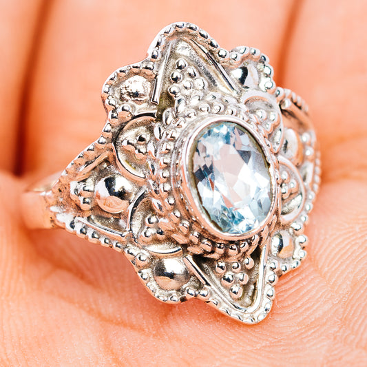 Sterling silver filigree ring with oval blue gemstone and carved side details, angled view