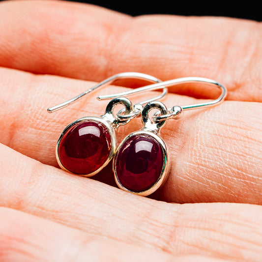 Red oval ruby earrings in .925 sterling silver, shown on hand with hook closures.