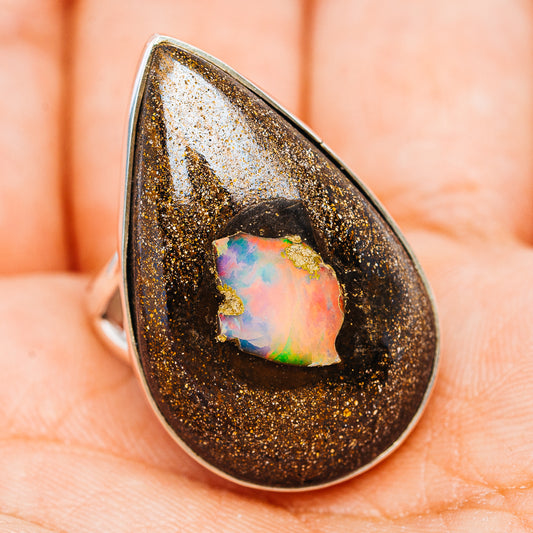 Teardrop opal ring on finger, dark gold-sparkle bezel with iridescent cabochon