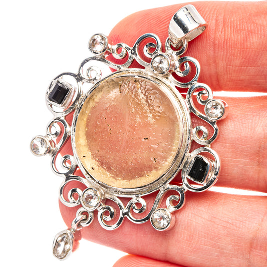 Round Libyan Desert Glass pendant with ornate silver frame, dark stones and clear accents