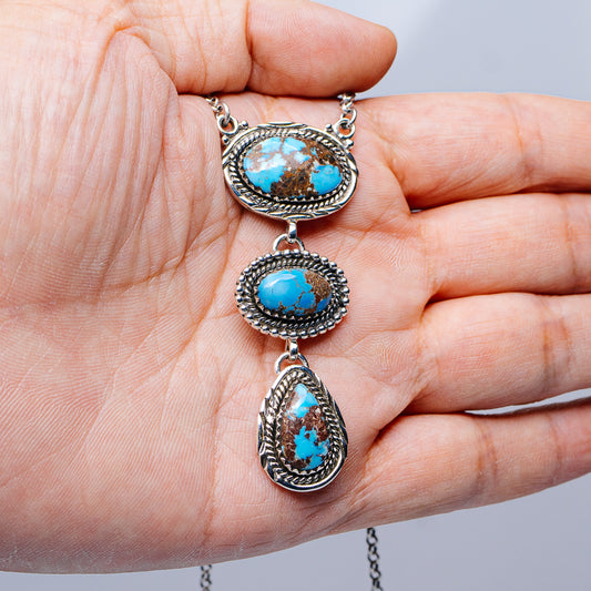Turquoise oval pendant necklace held up, three charms with beaded sterling silver borders