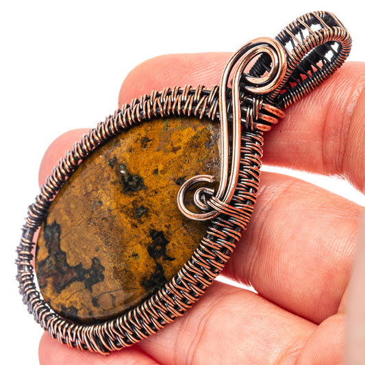 Oxidized copper wire-wrapped agate pendant in hand, oval stone with bail loop