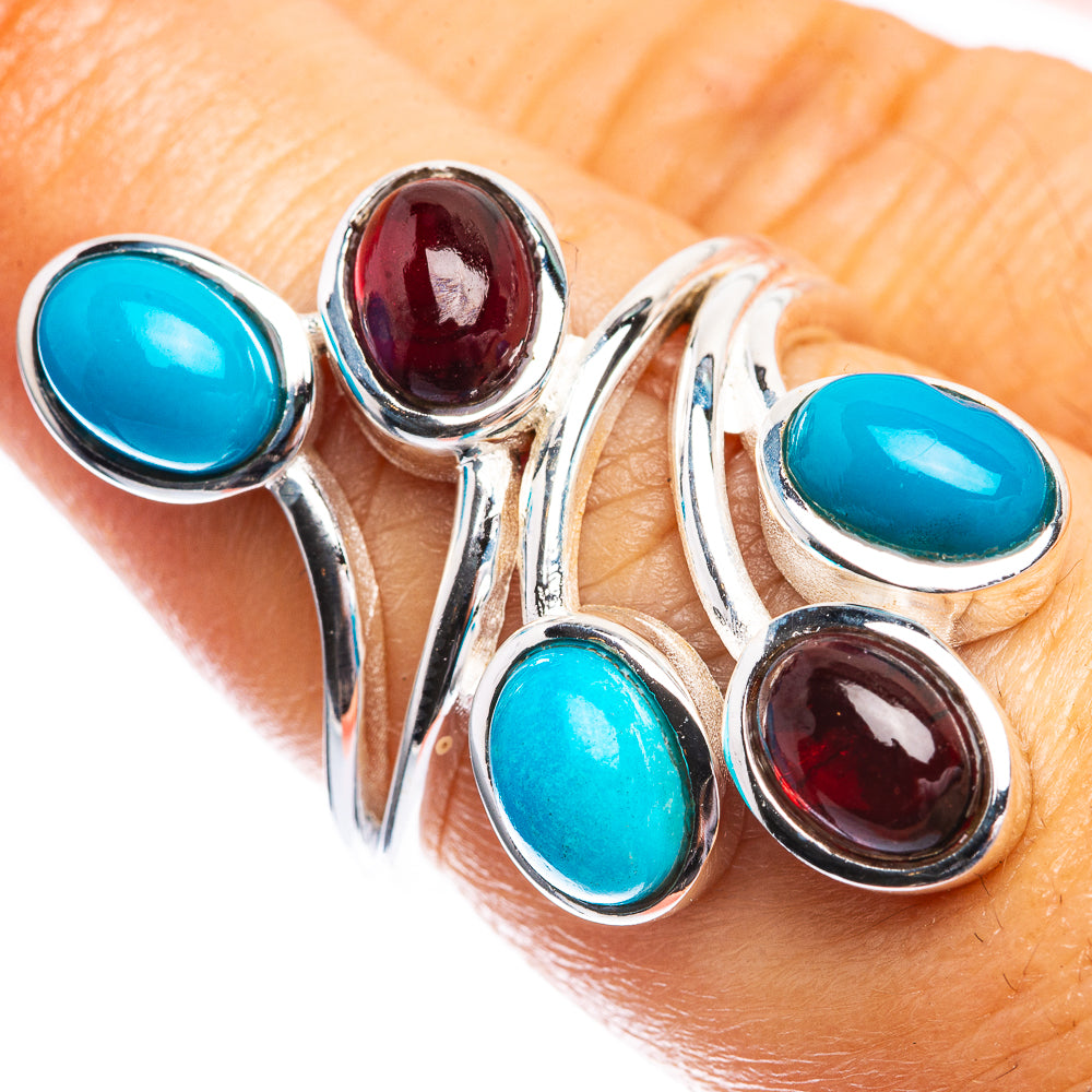 Turquoise-blue and garnet-red oval gemstone ring on finger, sterling silver band