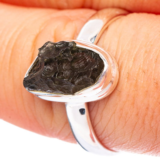 Sterling silver bezel ring with rough dark moldavite stone, worn on a finger