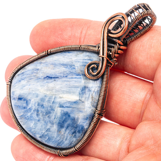 Kyanite wire-wrap pendant, oxidized copper bail and teardrop blue stone held in hand