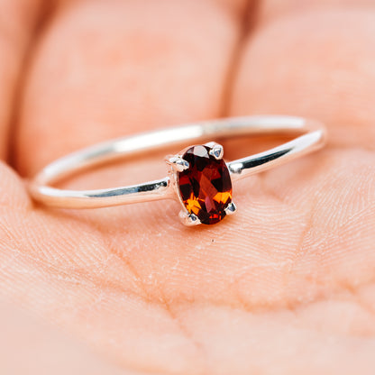 Sterling silver stackable ring with oval garnet gemstone, straight-on close-up on finger