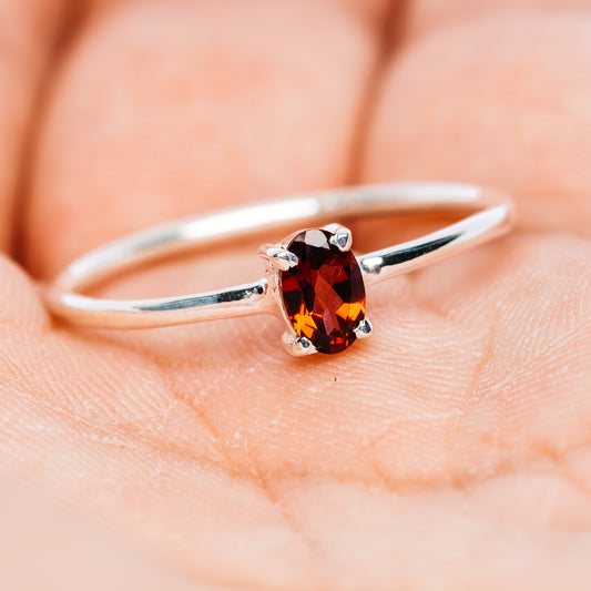 Sterling silver stackable ring with oval garnet gemstone, straight-on close-up on finger