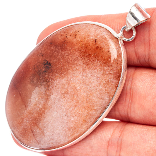 Sunstone pendant in hand, oval orange-pink cabochon with silver-plated bail