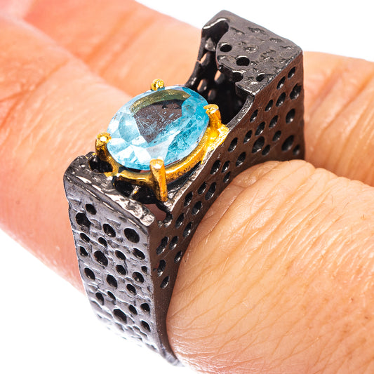 Blackened silver ring on finger with oval blue gemstone and cutout side band