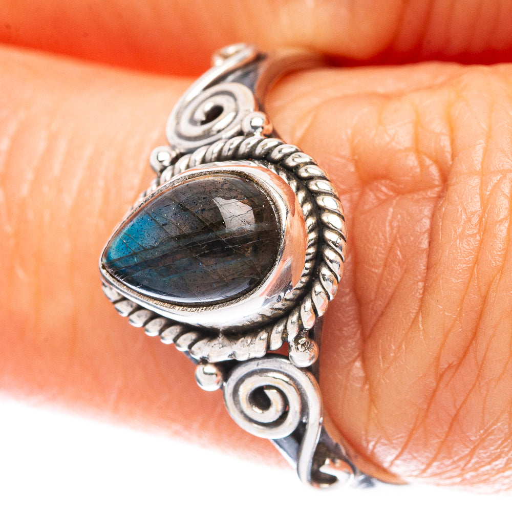 Sterling silver labradorite ring on finger; oval blue-green cabochon in braided border