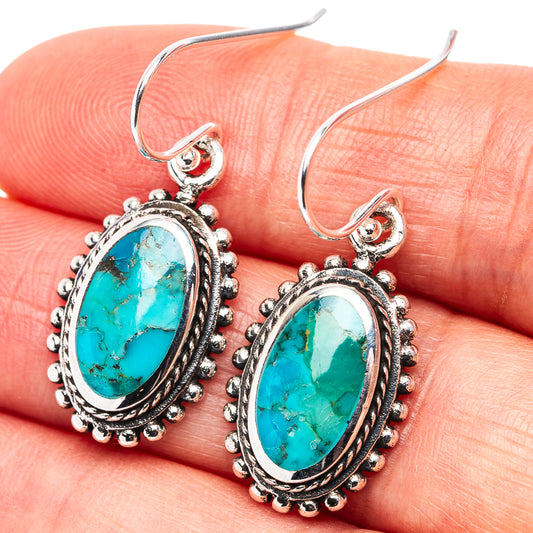 Turquoise oval drop earrings with ornate .925 sterling silver settings, shown on hand