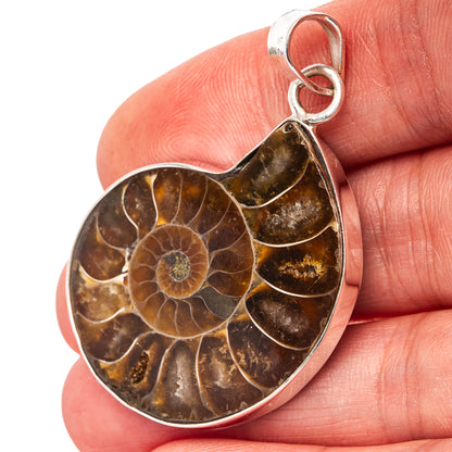 Ammonite fossil heart pendant with silver bail, shown on a hand for scale