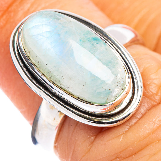Oval moonstone ring on finger, light blue stone in silver double-edge bezel