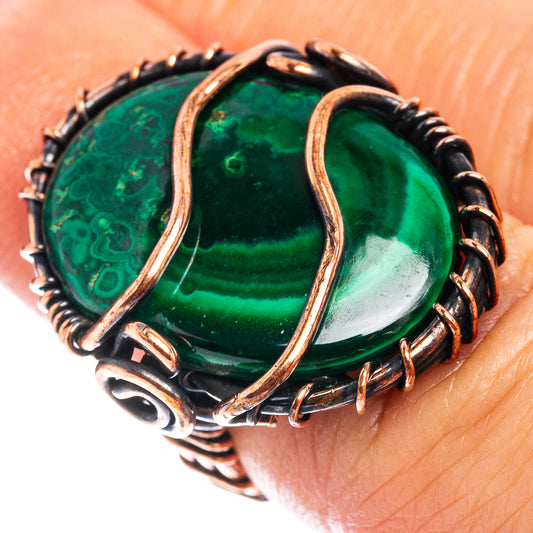 Oxidized copper wire wrap ring with oval green malachite stone on finger.