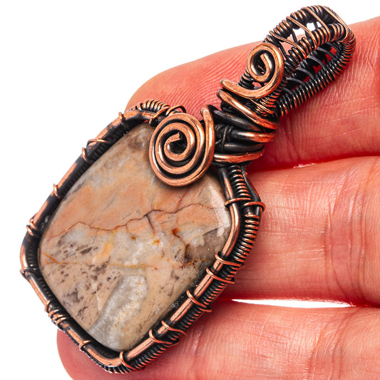 Oxidized copper wire-wrapped pendant with pale stone center and spiral accents