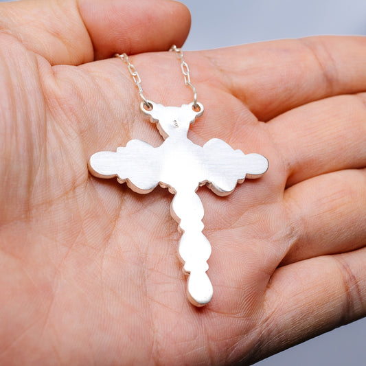 Silver cross pendant necklace with cutout textured design on chain, held in hand