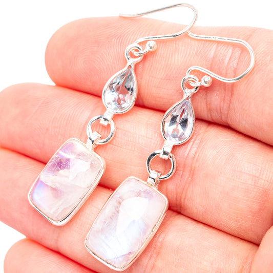 Sterling silver rainbow moonstone and blue topaz drop earrings, close-up on fingers