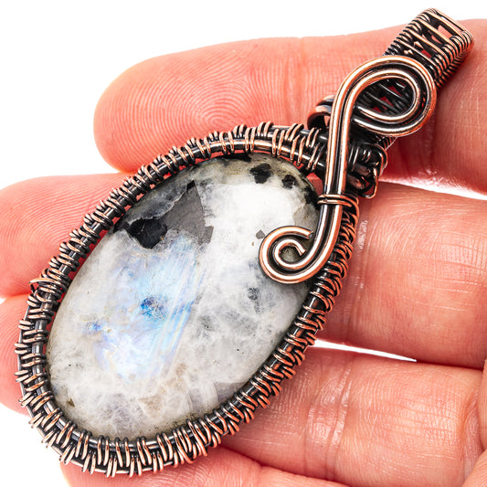 Close-up oval wire-wrapped moonstone pendant with black tourmaline in copper loops