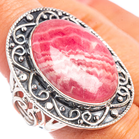 Oval pink rhodochrosite sterling silver ring on finger, ornate scrolling setting