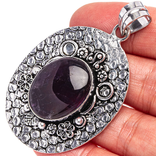 German silver amethyst pendant with oval purple cabochon and ornate floral border, bail top