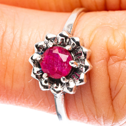 Sterling silver ring on fingertip, pink-red round gemstone with decorative cluster setting