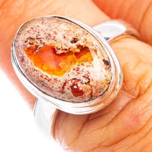 Sterling silver oval fire opal ring on finger, orange center with mottled brown matrix