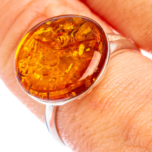 Oval amber cabochon sterling silver ring on finger, warm honey color