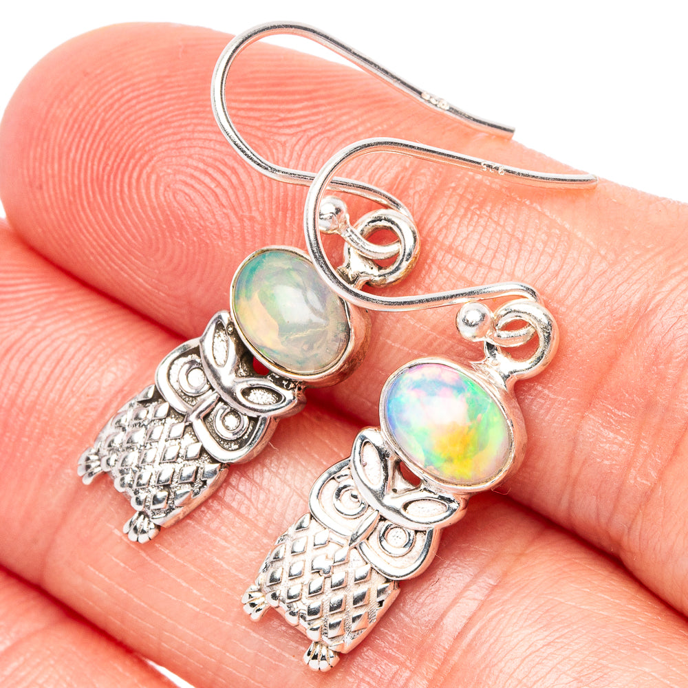 Close-up of sterling silver owl earrings with iridescent opal accents and lattice pattern