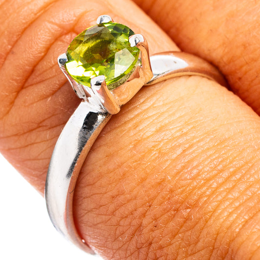Faceted oval green peridot gemstone in silver prong ring, close-up on finger