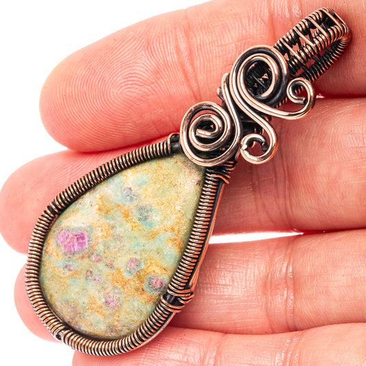 Oxidized copper wire wrap pendant with oval green stone and pink flecks, close-up bail