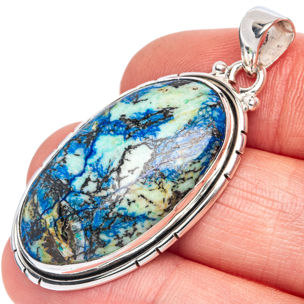 Oval sterling silver pendant on gemstone showing blue and green veining, held on fingertip