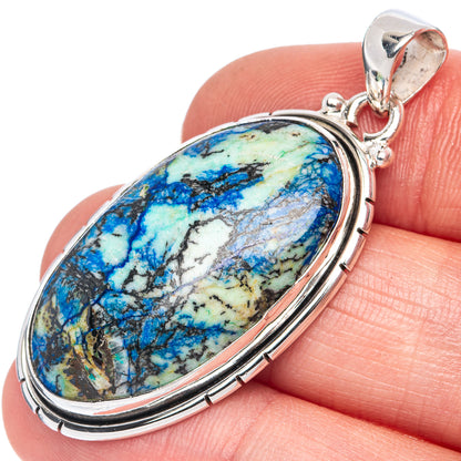 Oval sterling silver pendant on gemstone showing blue and green veining, held on fingertip