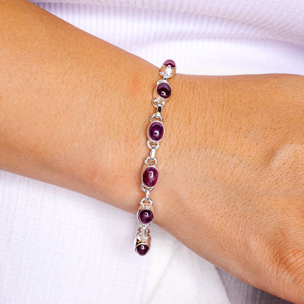 Sterling silver ruby bracelet with oval dark red gemstones, close-up on wrist