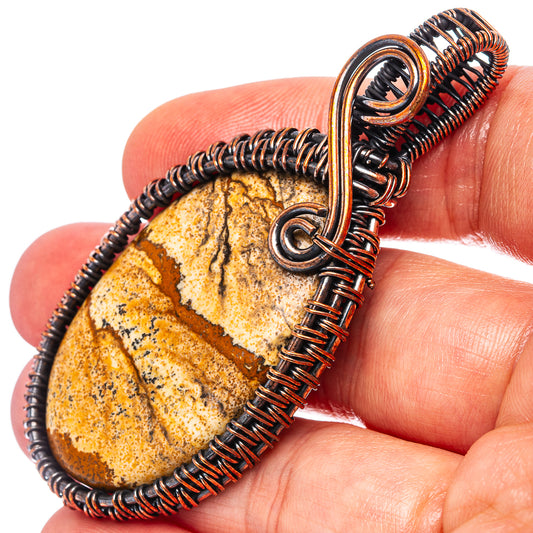 Oxidized copper wire-wrapped picture jasper teardrop pendant on a finger
