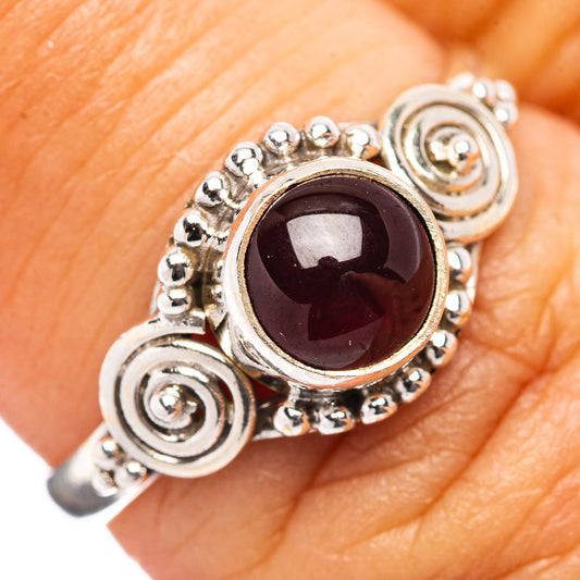 Sterling silver garnet ring on finger with round dark red gemstone and spiral details