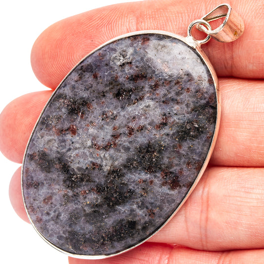 Silver-plated oval palm stone pendant with dark gray-purple speckled stone, held on finger