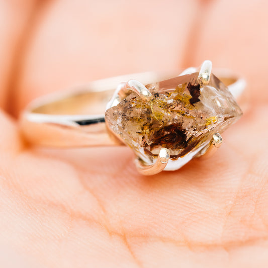 Side view of a sterling silver ring with a raw quartz stone and dark brown inclusions
