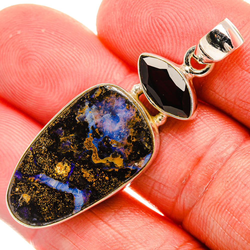 Close-up teardrop boulder opal and red garnet pendant on sterling silver