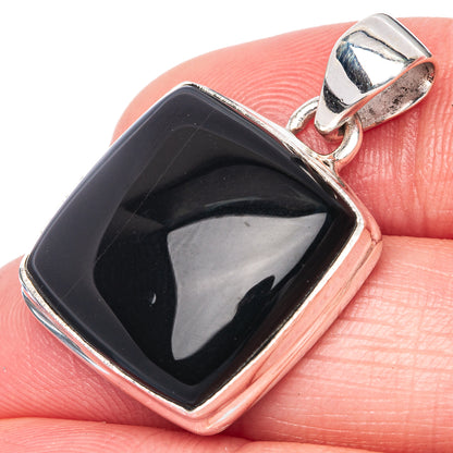 Black onyx pendant with square silver bezel and top loop, on fingertip