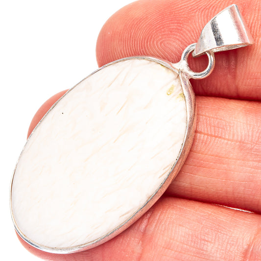 Oval scolecite pendant with silver-plated bail and pale white gemstone, shown on finger.