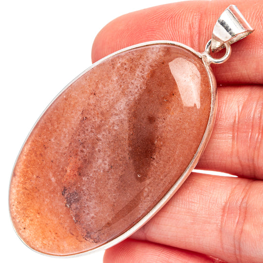 Silver-plated sunstone oval pendant held in hand; reddish orange stone in bezel