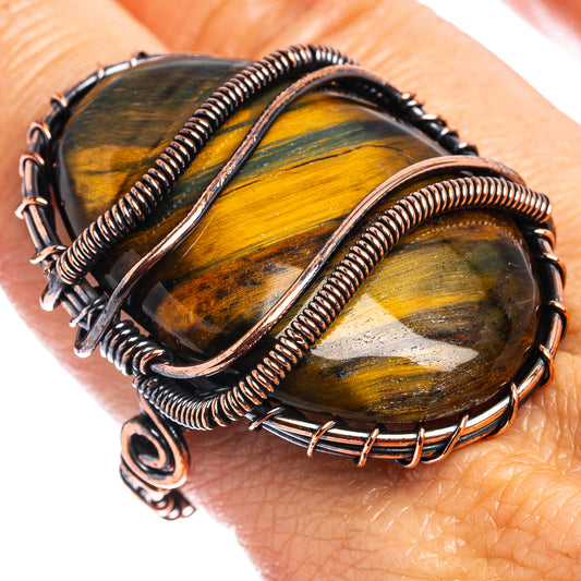 Oxidized copper wire-wrap ring on hand, showing blue-gold oval tiger eye stone