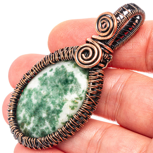 Close-up moss agate wire-wrapped pendant with oxidized copper wire spirals and green stone
