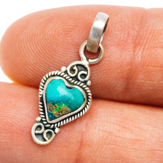 Sterling silver turquoise heart pendant with ornate border and bail, on fingertip