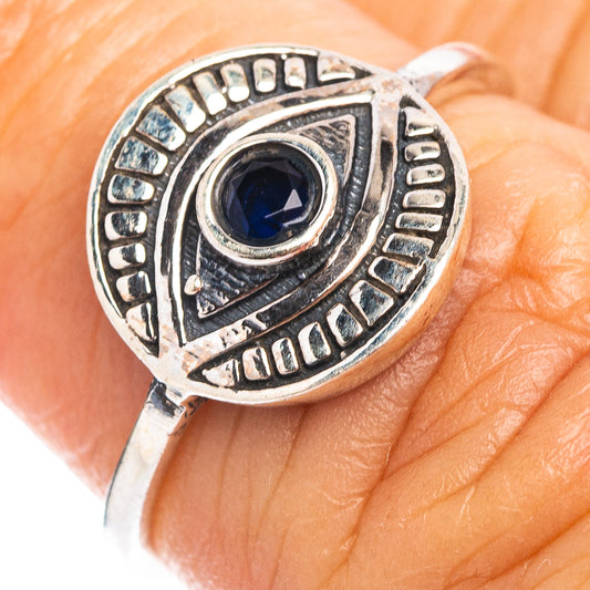 Sterling silver eye ring with dark blue gemstone on finger, ornate engraved band.