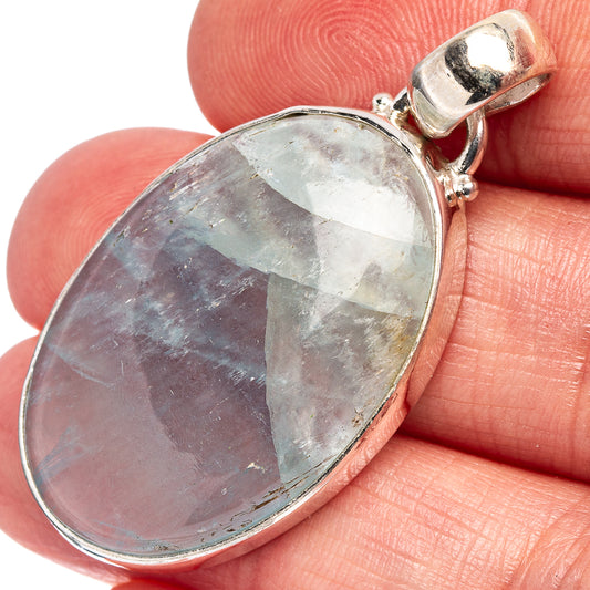 Oval aquamarine pendant in .925 sterling silver bezel on finger, faceted light-blue stone