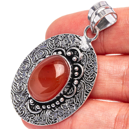 Silver-toned teardrop pendant with pink-red opal cabochon and ornate filigree border