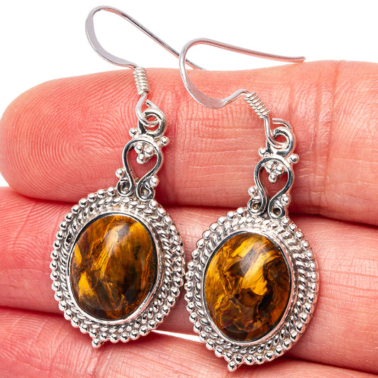 Closeup of sterling silver drop earrings with amber-gold oval pietersite stones and textured border