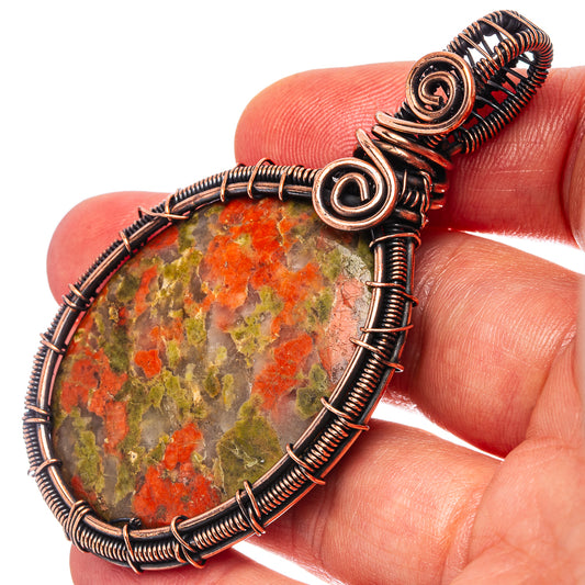 Unakite wire-wrap pendant close-up on oxidized copper coils and oval stone, held by hand