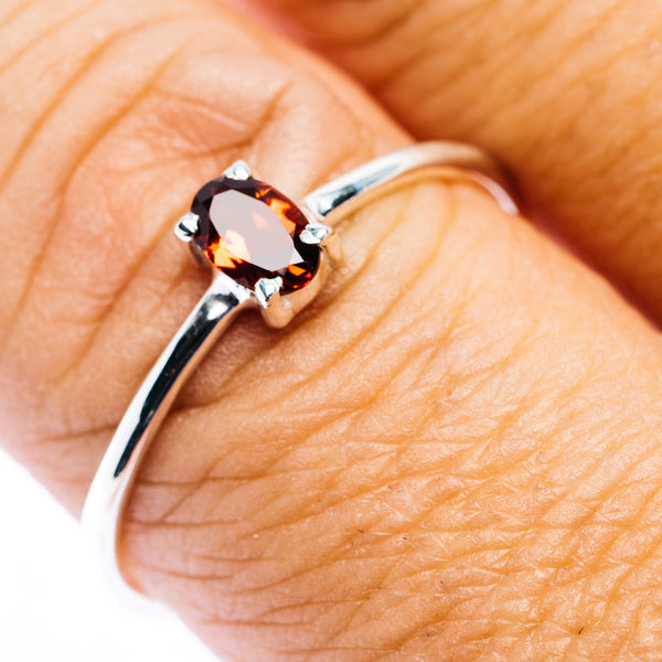Sterling silver stackable ring with oval garnet gemstone, angled close-up on finger